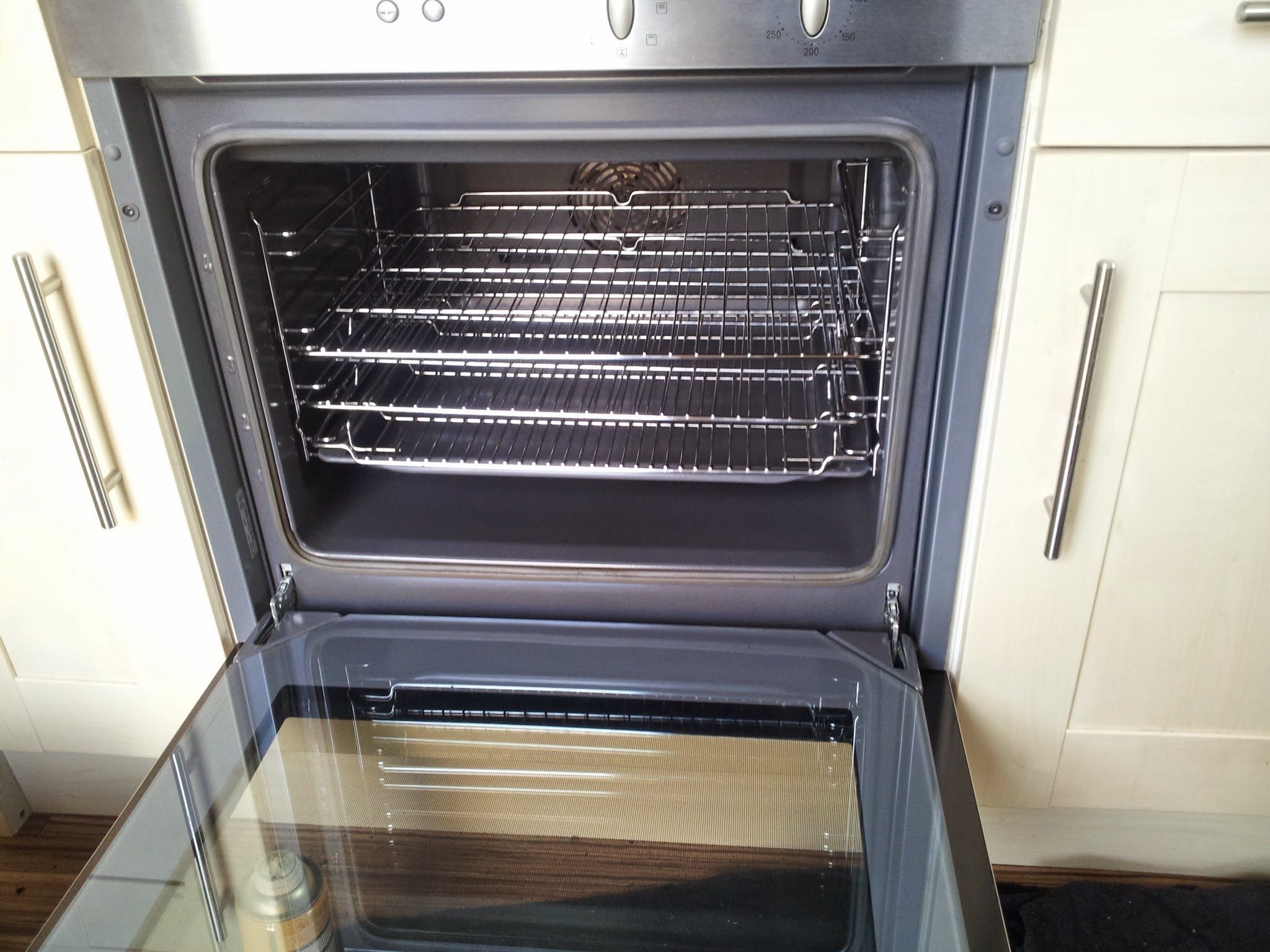 A built-in oven after cleaning, door open with spotless glass and shining racks